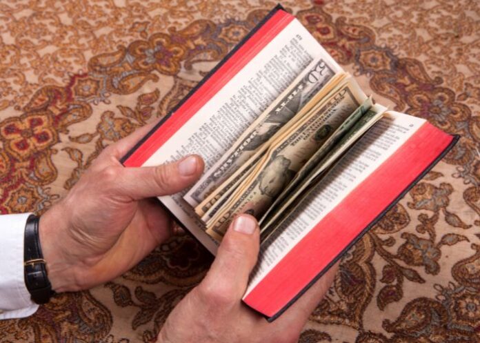 Mãos segurando uma Bíblia com dinheiro (Imagem ilustrativa)
