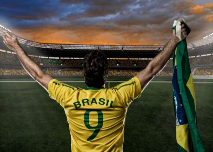 Jogador com a camisa da seleção brasileira e segurando a bandeira do Brasil (Foto: Canva Pro)