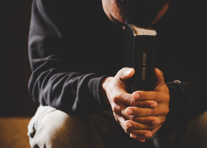 Homem orando com uma Bíblia na mão (Foto: Canva Pro)